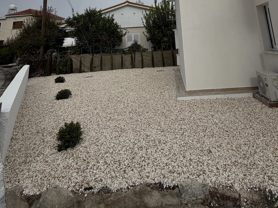 Μετά: η ίδια αυλή με λευκό τσακκίλι, θάμνους και κυπαρίσσια